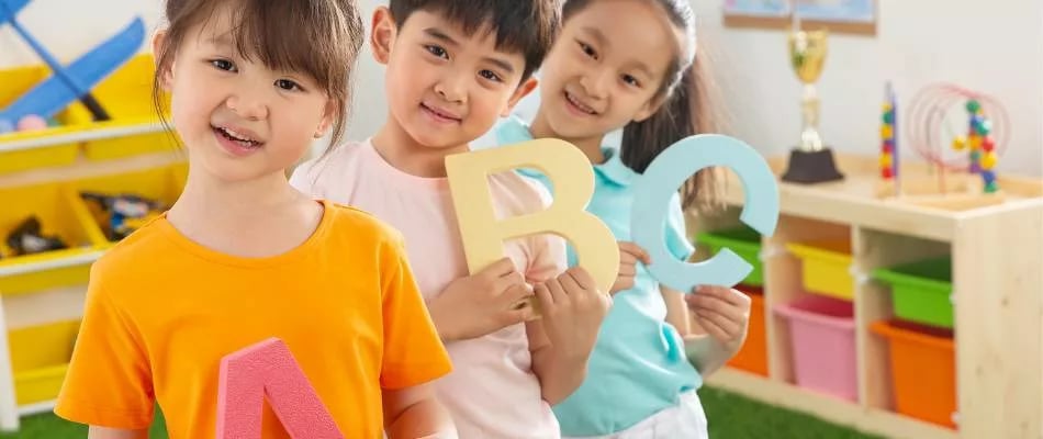 Benefits of mastery-based learning shown by happy children holding alphabet letters in a colorful, engaging classroom setting.