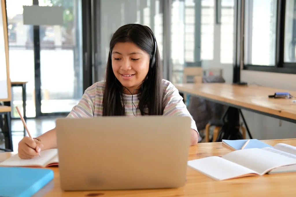 Remote learning student smiling while taking notes and watching a lesson on a laptop at a shared workspace