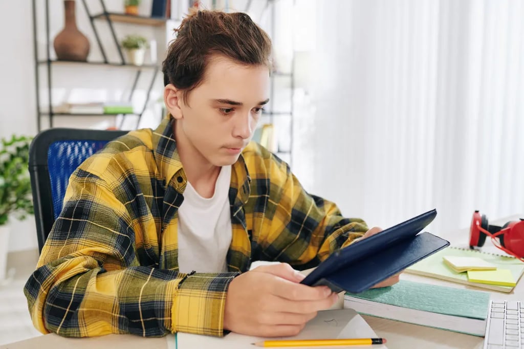 Self-directed learning in homeschool with a teenage boy focused on studying independently using a tablet at his desk