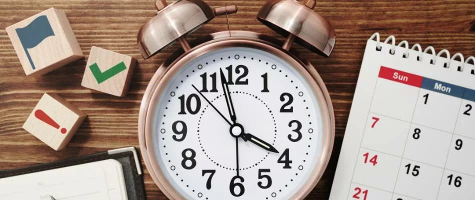 Effective time management strategies represented by a clock, calendar, and planning blocks on a wooden desk.