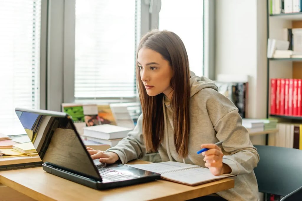 A focused student works on a laptop while taking notes, engaging in student-centered learning at her desk