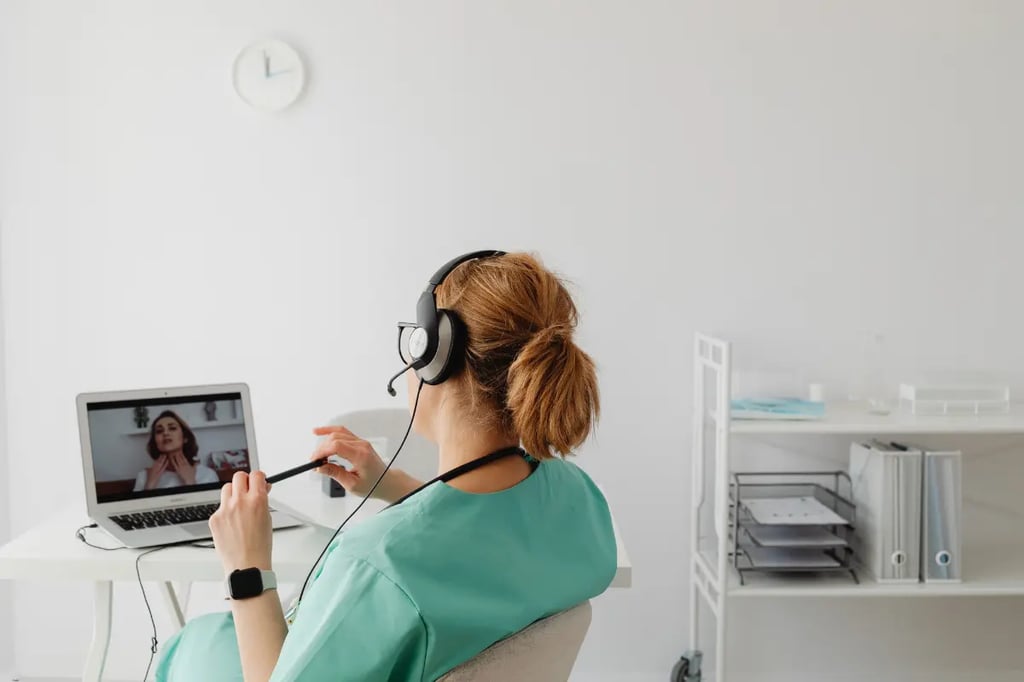 Online private homeschool tutor in scrubs attending a virtual session with a student on a laptop in a minimal workspace.