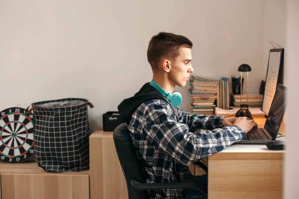 Online homeschool high school student studying at a desk with a laptop in a cozy bedroom setup.