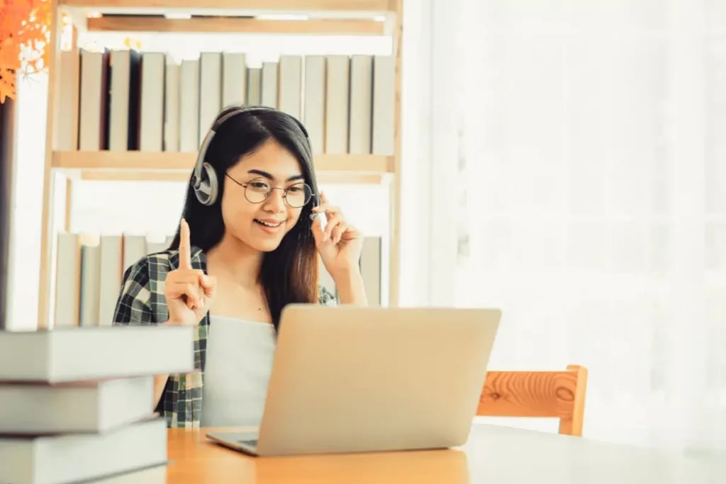 Online middle school homeschool student engaged in a virtual class while wearing a headset and sitting at a desk with books.