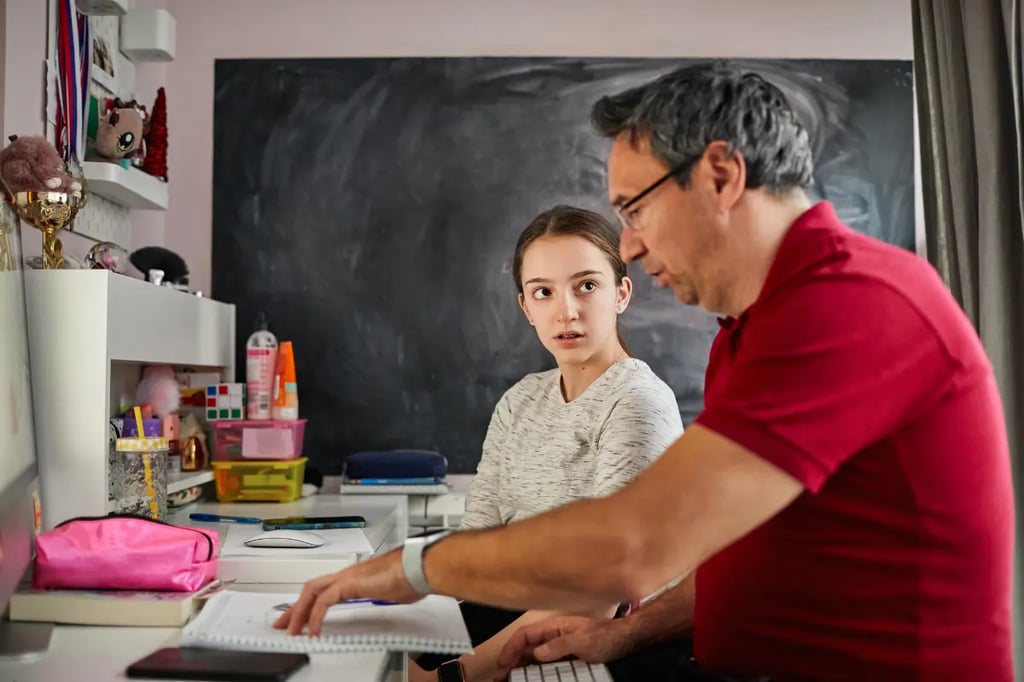 Online accredited homeschool session with a father helping his daughter study at a desk with books and a computer