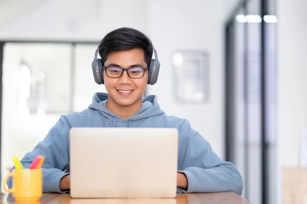 A young man wearing headphones studies on his laptop, participating in a private online homeschool program