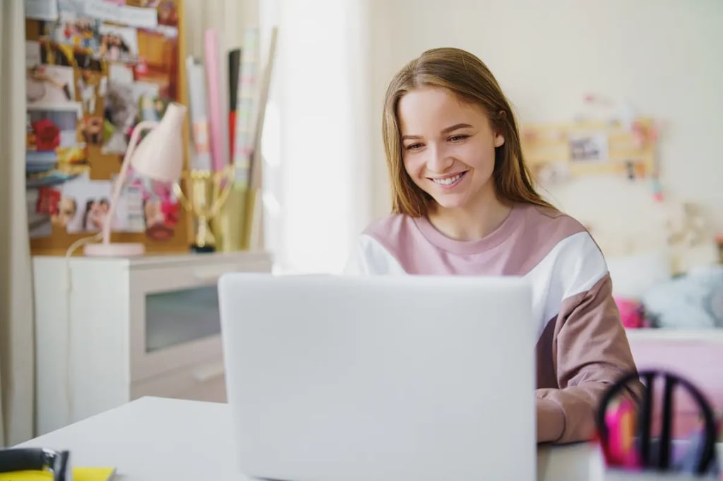 Online private school student smiling while learning from a laptop in a decorated bedroom study space.