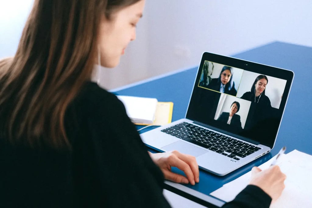 Virtual learning session with a woman taking notes during a video conference on her laptop.