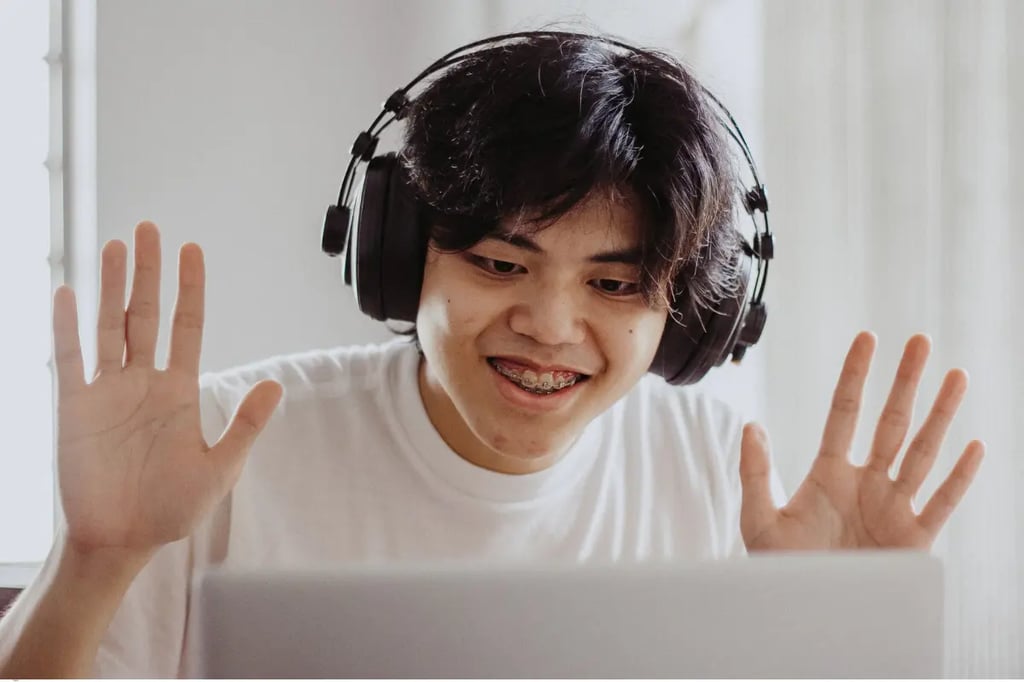 Online homeschool student wearing headphones and smiling while participating in a virtual class on a laptop