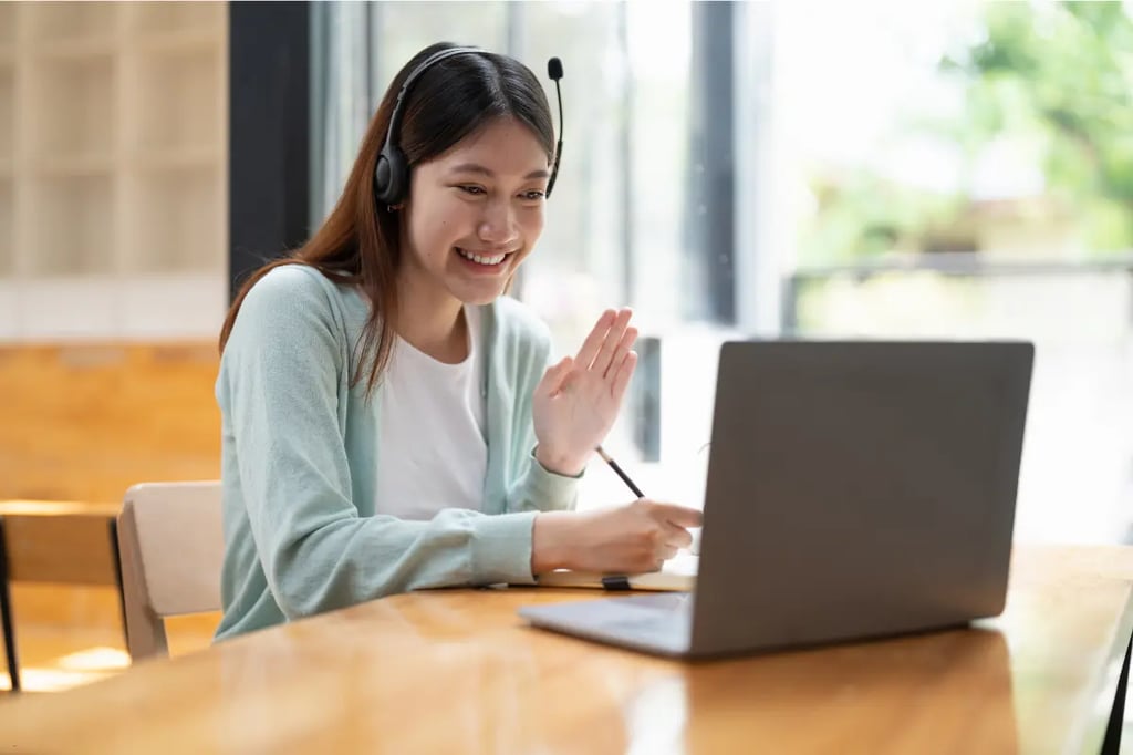 A woman waves and smiles during a virtual lesson on her laptop, participating in private online homeschool