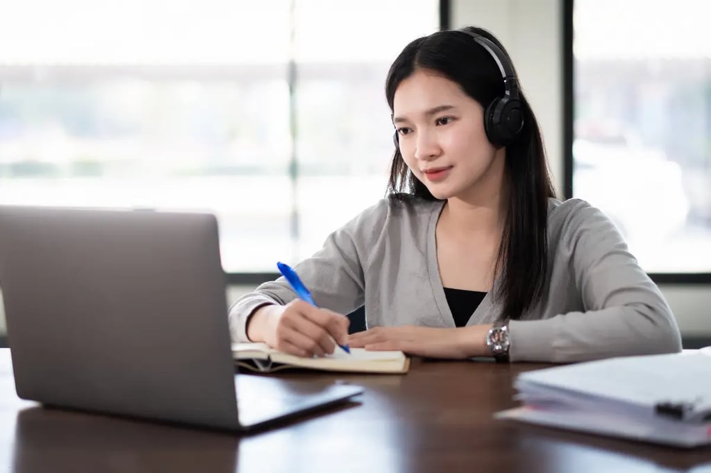 Accredited online homeschool curriculum student taking notes while attending an online class with a laptop and headphones.