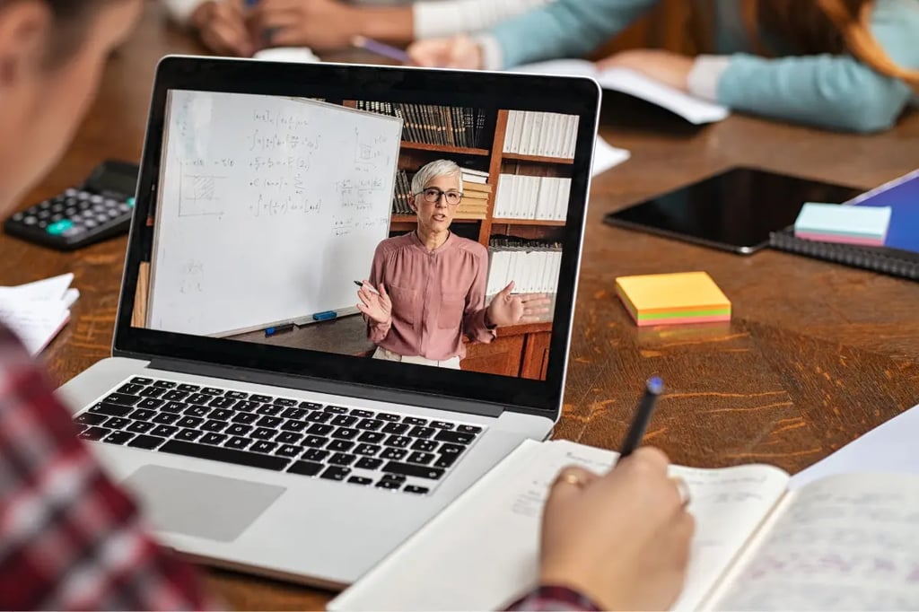 Accredited homeschool student taking notes during an online math lesson with a teacher on a laptop screen