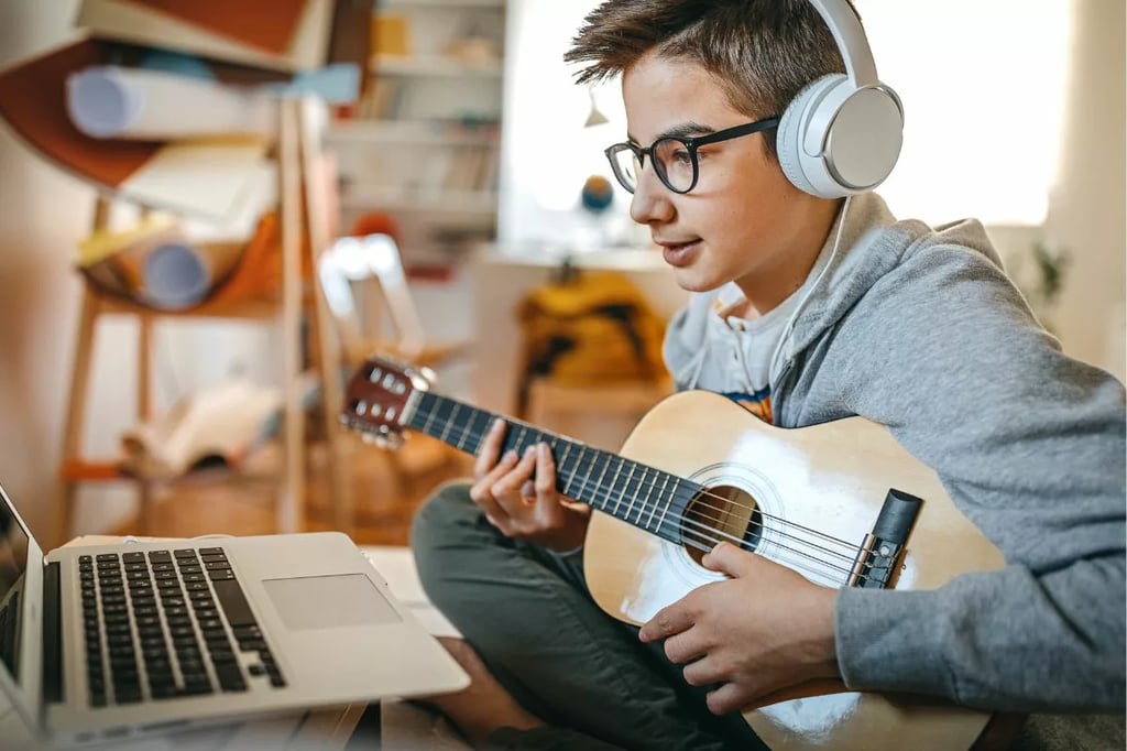 Best virtual high schools depicted by a teen learning guitar online with headphones and a laptop in a cozy room
