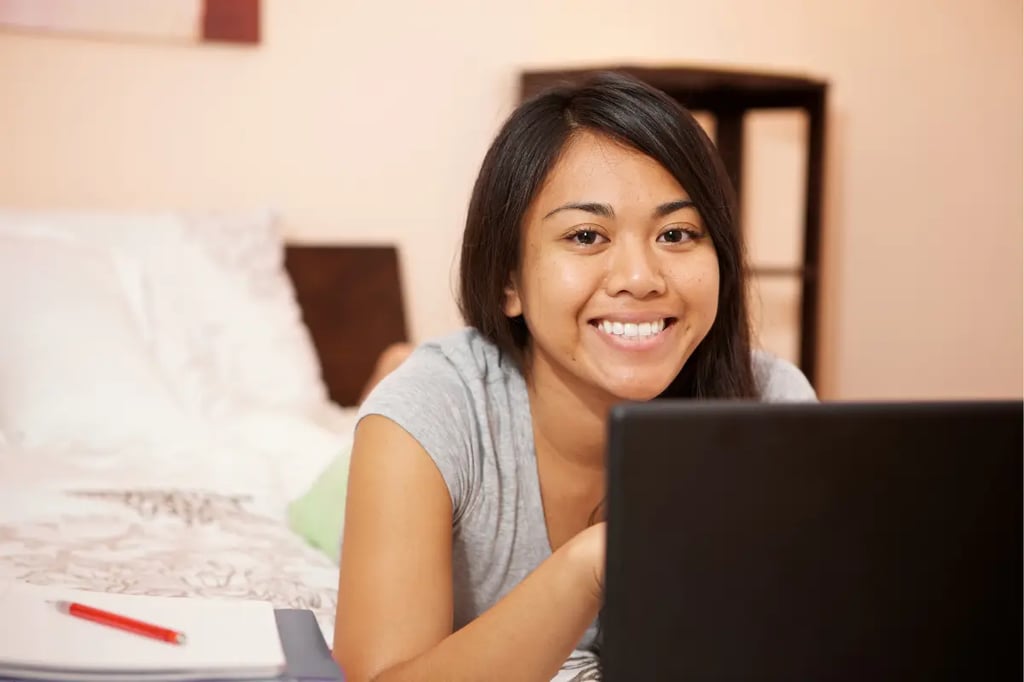 Engagement in virtual learning highlighted by a cheerful student using a laptop on a bed with notebooks.