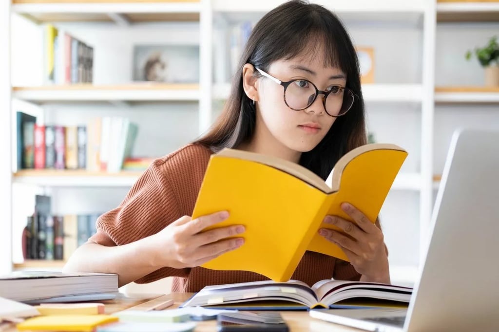 Online high school programs support focused learning as a student studies with books and a laptop at home.