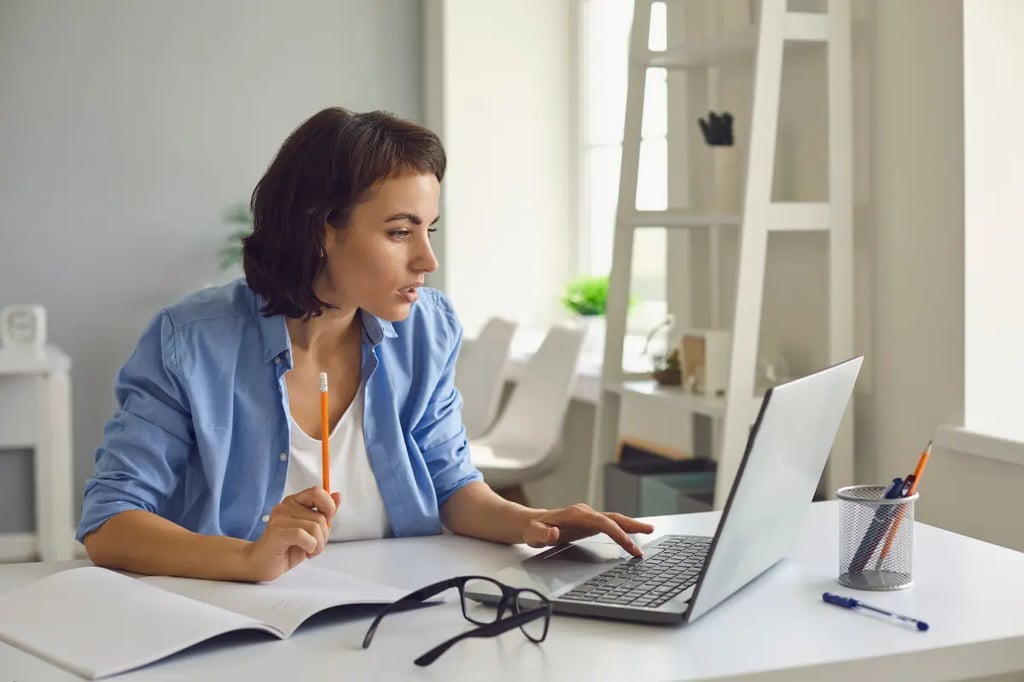 Online homeschool curriculum in use as a woman studies with a laptop and notebook at her desk.