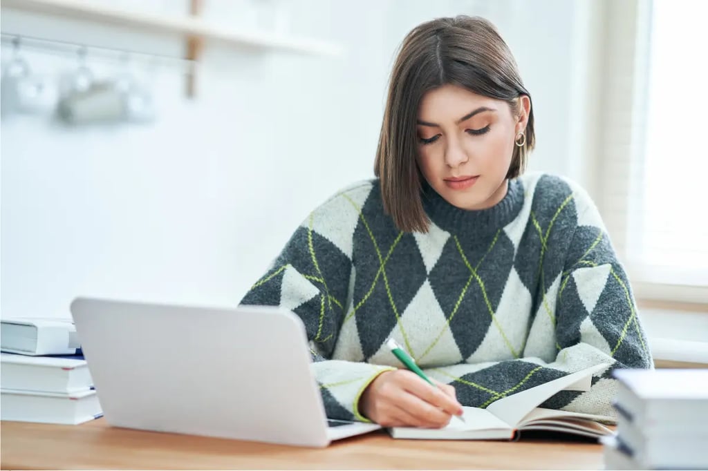 Online homeschooling with a student writing notes while studying on a laptop at home.