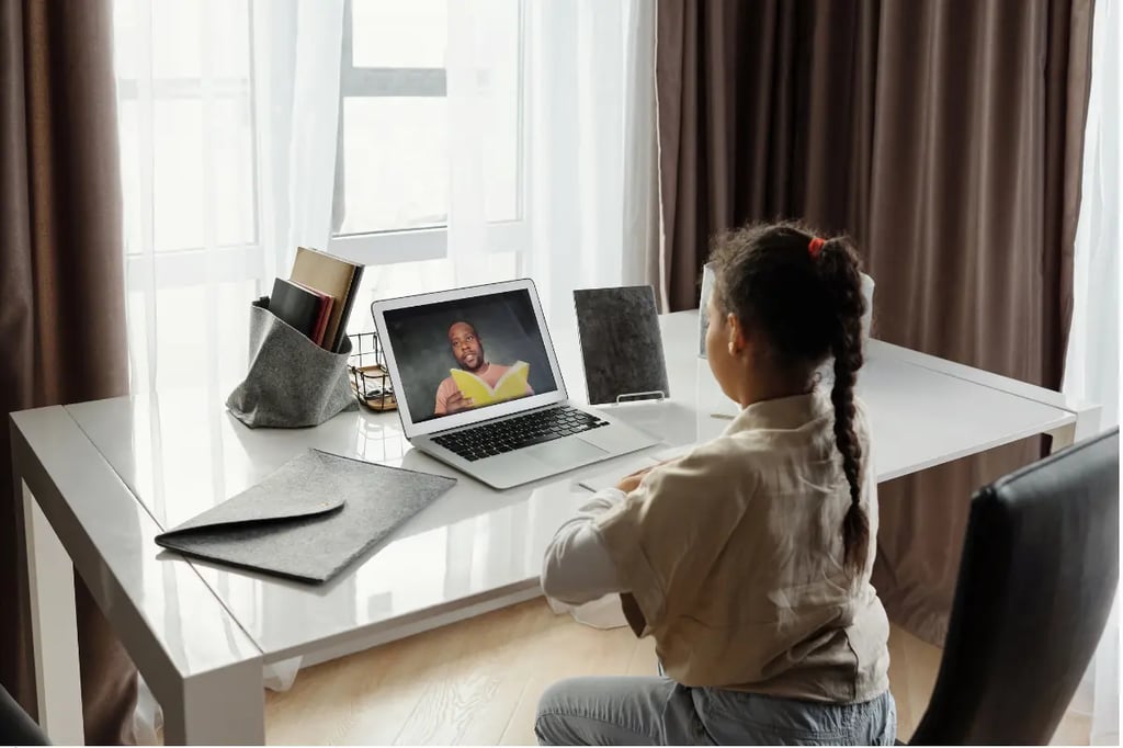 Private virtual school child watching an online lesson with a teacher reading a book on a laptop screen.