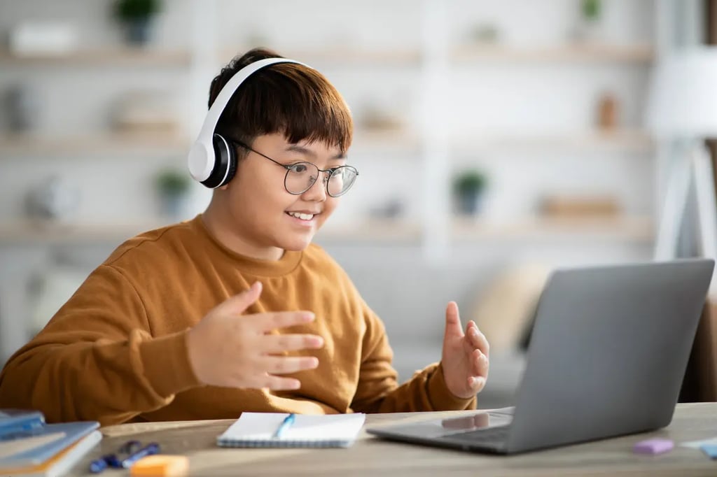 Private virtual school student wearing headphones and engaging in a video lesson with a laptop and notebook.