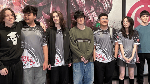 Online homeschool students pose together, some wearing matching esports jerseys, in front of a gaming-themed backdrop.
