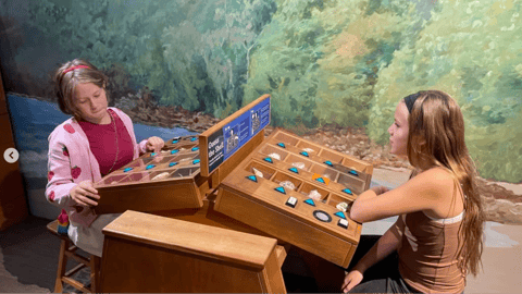 Two young girls explore a wooden display of minerals and gemstones in an interactive nature exhibit.