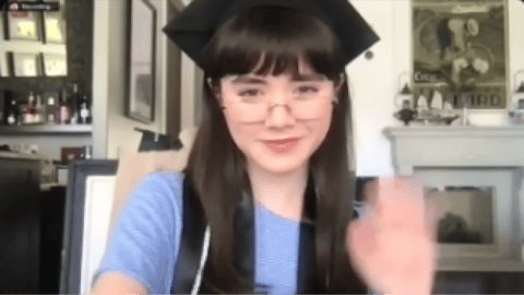 Online homeschool for high school graduate wearing a cap and gown waves during a virtual graduation celebration at home.