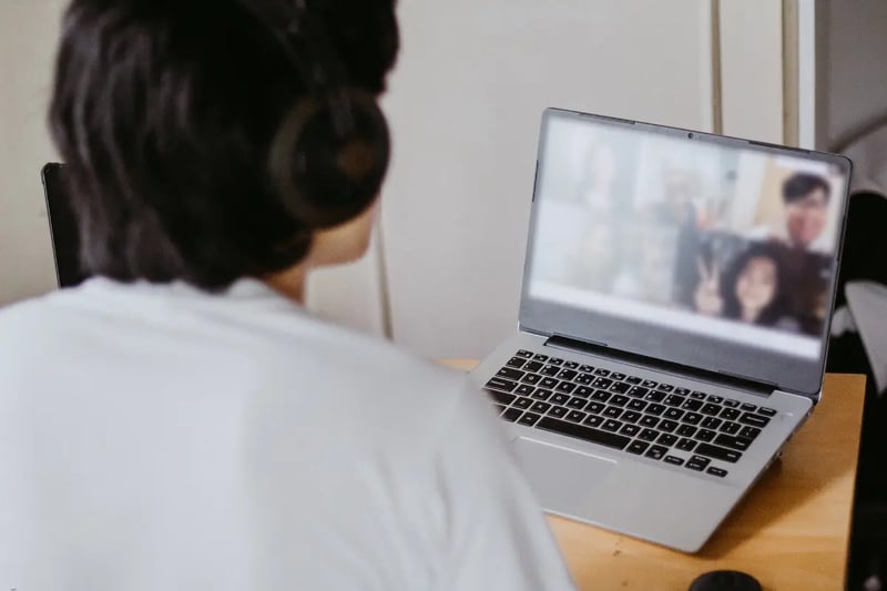 Student attending an online homeschool class, wearing headphones and interacting with peers on a laptop