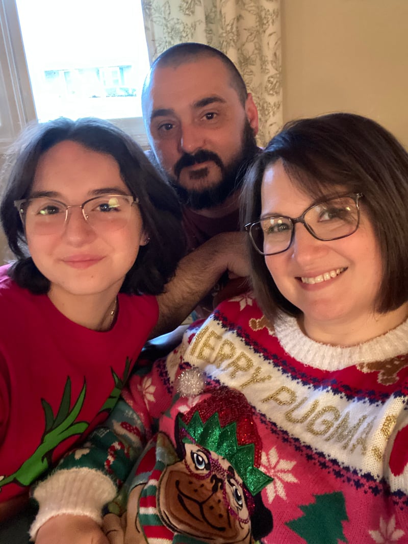 A smiling family wearing festive Christmas sweaters poses together indoors for a holiday photo.