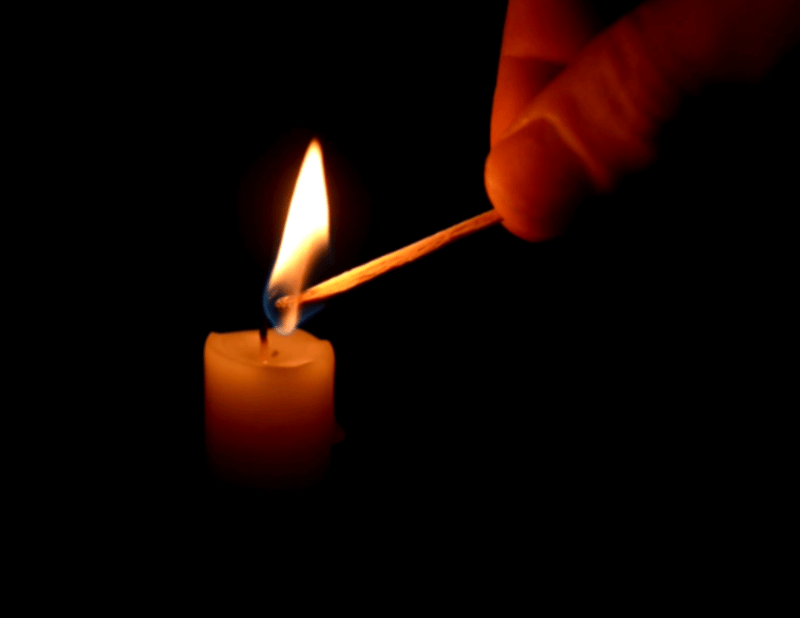 A hand lighting a candle with a match in a dark setting, creating a warm glow.