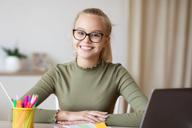 Interest-based online learning setup with a smiling student using a laptop and colorful study supplies.