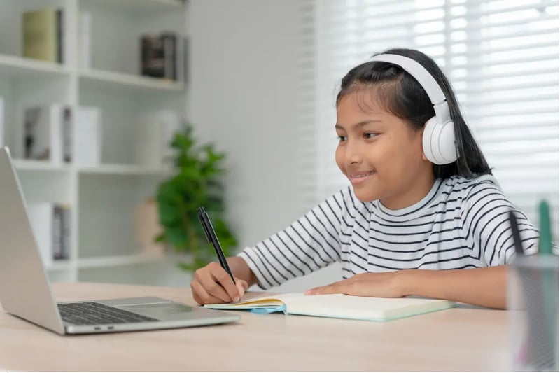 Private online homeschool programs student wearing headphones and studying with a laptop and notebook.
