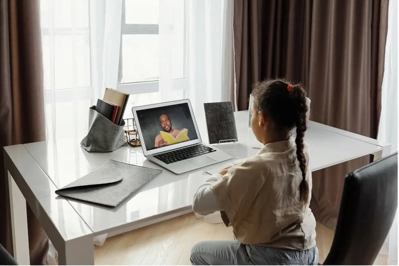 Private virtual school child watching an online lesson with a teacher reading a book on a laptop screen.